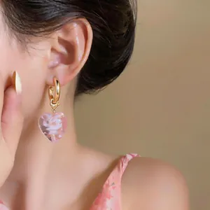 Close-up view of elegant pink heart glass bead earrings with gold hoops worn by model