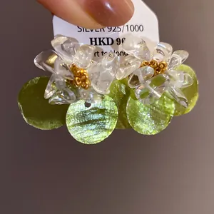 Detail of silver needle earrings with clear gravel petals and green shell disks