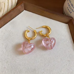 Close-up of pink glass heart earrings with gold hoops on a textured background fabric