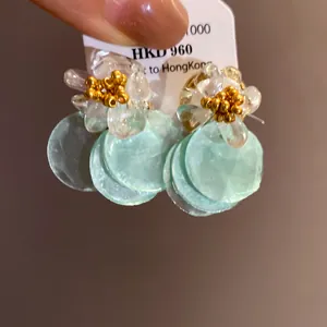 Detail view of floral stud earrings with mint green shell discs and gold beads.