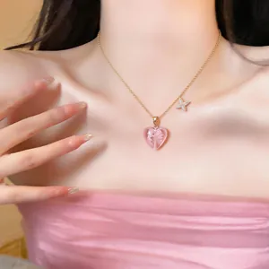 Close-up view of a pink heart pendant necklace with a gold chain worn by a model