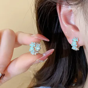 Detailansicht von blauen Emaille-Blumenohrringen mit Zirkonia, getragen von einem Modell.