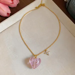 Detail view of a gold-plated heart necklace with a pink glass pendant and flower charm