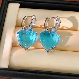Close-up of silver-tone hoop earrings featuring large light blue heart-shaped crystals.