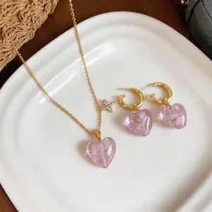 Detail view of pink glass heart pendants and gold chains on a white ceramic dish
