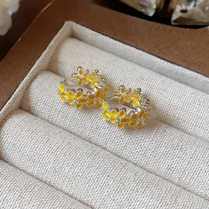 Nahaufnahme silberner Creolen mit gelben Emaille-Blumen und funkelnden Zirkonen.