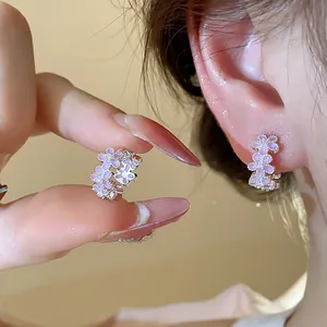 Nahaufnahme von rosa Emaille-Blumenohrringen mit Zirkon-Details am Ohr des Modells