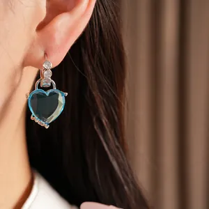 Close-up detail of a blue heart-shaped crystal earring with zircon accents on an ear.