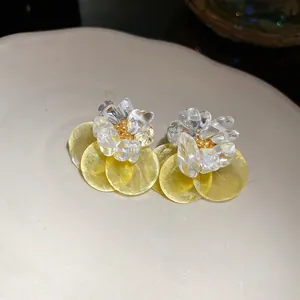 Close-up detail of summer vacation style earrings with yellow shell discs and clear crushed stones.