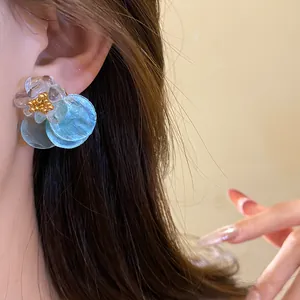 Close-up view of elegant summer blue shell disc earrings with flower detail worn on ear.