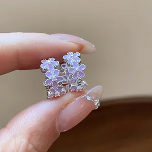 Nahaufnahme eleganter Ohrringe mit lila Blumen und glänzenden Zirkonia-Verzierungen.