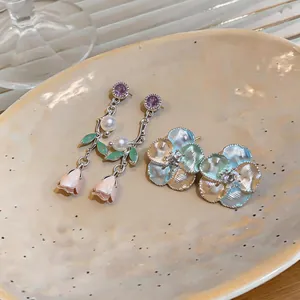 Detail shot of elegant enamel flower and pearl dangle earrings on a ceramic plate