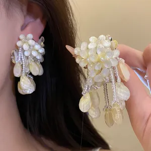 Detailaufnahme eleganter cremefarbener Perlenblumen-Ohrringe mit Quastenverzierung.