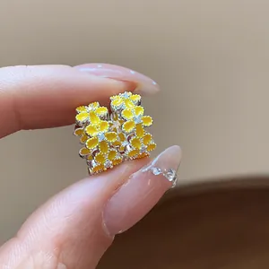 Makro-Detail von gelben Emaille-Blumenohrringen mit funkelnden Zirkonia-Akzenten.