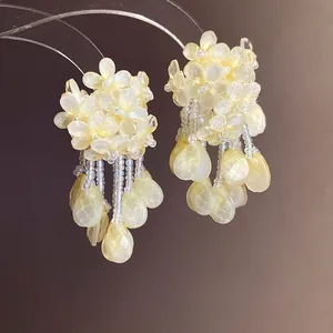 Detailansicht gelber Perlenohrringe mit Blumen und durchsichtigen Quastenanhängern.