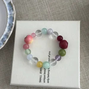 Close-up detail of a colorful beaded resin bracelet with apple charms on white gift box
