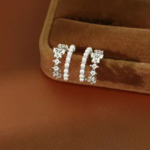 Detail view of silver-toned double-layered C-shaped earrings with pearls and butterfly charm.