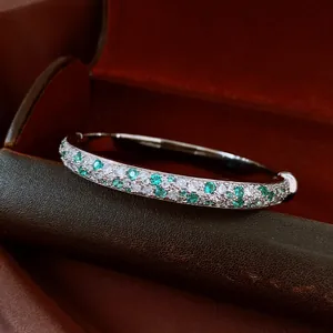 Detailed macro view of a silver-toned bangle set with mint green and white cubic zirconia stones.