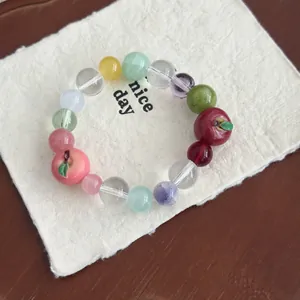 Macro detail of a colorful beaded bracelet featuring cute resin apple and peach charms.