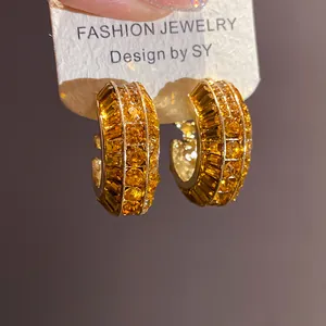 Primo piano di orecchini vintage a cerchio a C in oro con brillanti zirconi ambrati.