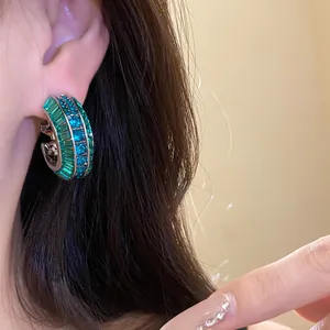 Primo piano di eleganti orecchini vintage a forma di C con zirconi verdi e blu brillanti.
