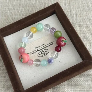 Macro detail of a sweet resin apple beaded bracelet displayed in a plush brown box