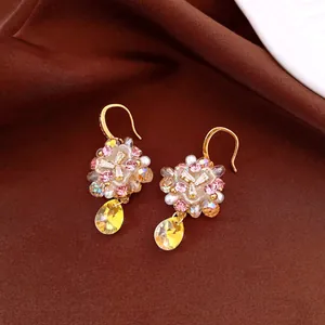 Macro detail of floral crystal earrings featuring pink zircons and large yellow teardrop pendant