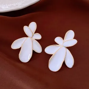 Detail view of elegant white petal flower stud earrings with gold trim on dark fabric