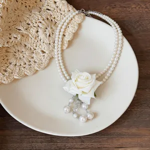 Vue détaillée d'un collier de perles à deux rangs avec rose en tissu et pompons.