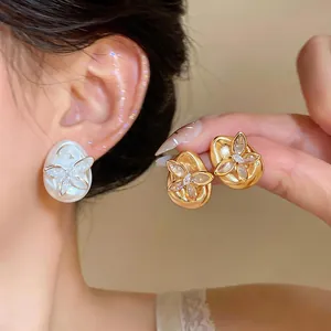 Close-up of elegant gold and pearl teardrop stud earrings with butterfly zircon detail