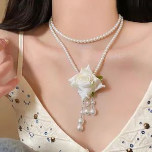 Gros plan sur collier de perles double épaisseur avec fleur en tissu blanc et franges.