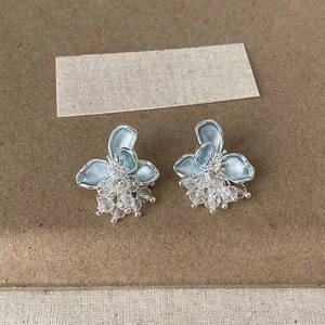 Dettaglio di orecchini a fiore in smalto blu con nappe di cristallo scintillanti.