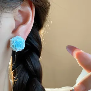 Close-up view of an elegant blue resin rose flower stud earring worn on the ear.