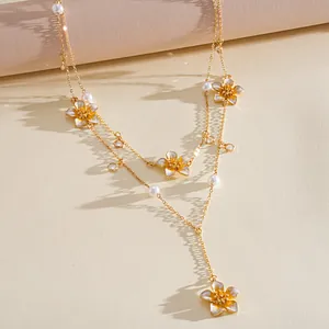 Detail view of a double-layered gold necklace with enamel flowers and pearls