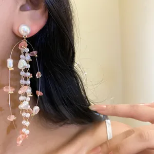 Close-up of elegant long pearl and peach stone tassel earrings worn by a model
