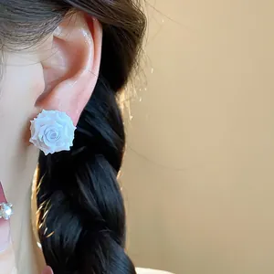 Close-up detail showing a white resin rose flower stud earring worn on an ear with braided hair