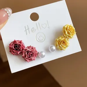 Detailed view of sweet French resin rose and pearl stud earrings on a white display card