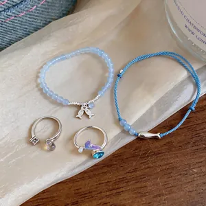 Close-up detail of light blue beaded fish bracelet and dainty silver rings on fabric