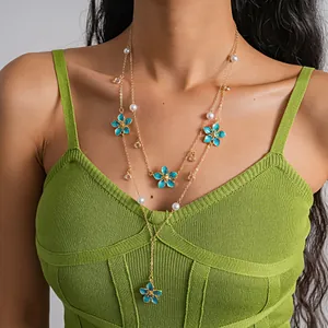 Detailed view of elegant two-layer gold necklace with blue enamel flowers and pearls on model