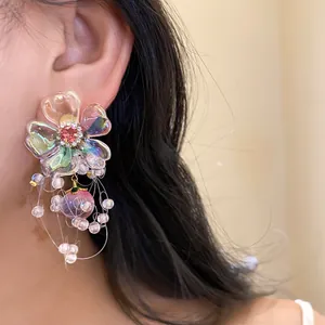 Close-up of iridescent flower earrings with pink zircon center and beaded peach tassel.