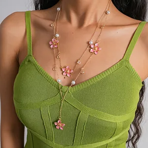 Close-up detail of a layered gold-tone necklace featuring pink enamel flowers and pearls.