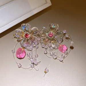 Macro detail of iridescent flower earrings featuring pink zircons and delicate beaded tassels.