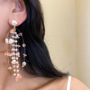 Close-up of elegant long tassel earrings featuring pearls and pink stones on a model