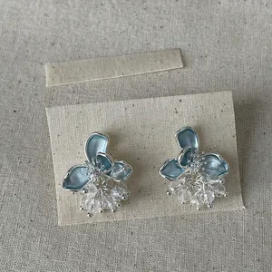 Dettaglio di eleganti orecchini a fiore in smalto blu con nappe di cristallo su lino.