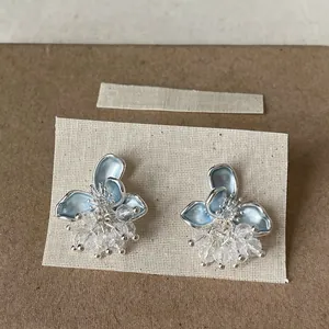 Dettaglio di eleganti orecchini a lobo a fiore blu con nappe di perline di cristallo.