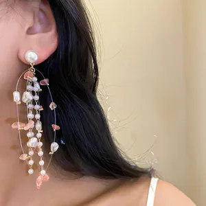 Elegant long tassel earrings featuring pearls and pink stones shown on a model's ear