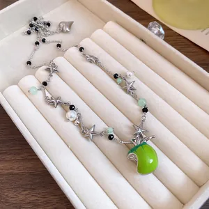 Vue détaillée d'un collier argenté avec pendentif pomme verte et breloques en étoile.