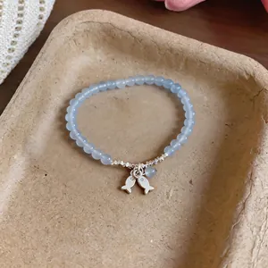 Detail shot of light blue beaded bracelet with cute silver fish charms.