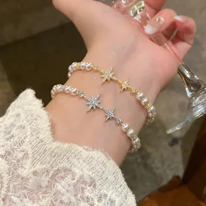 Elegant pearl bracelets with sparkling zircon star charms worn on a wrist holding a glass.