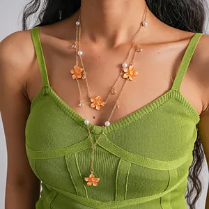 Detailed view of layered orange floral and pearl necklace on a model wearing green top